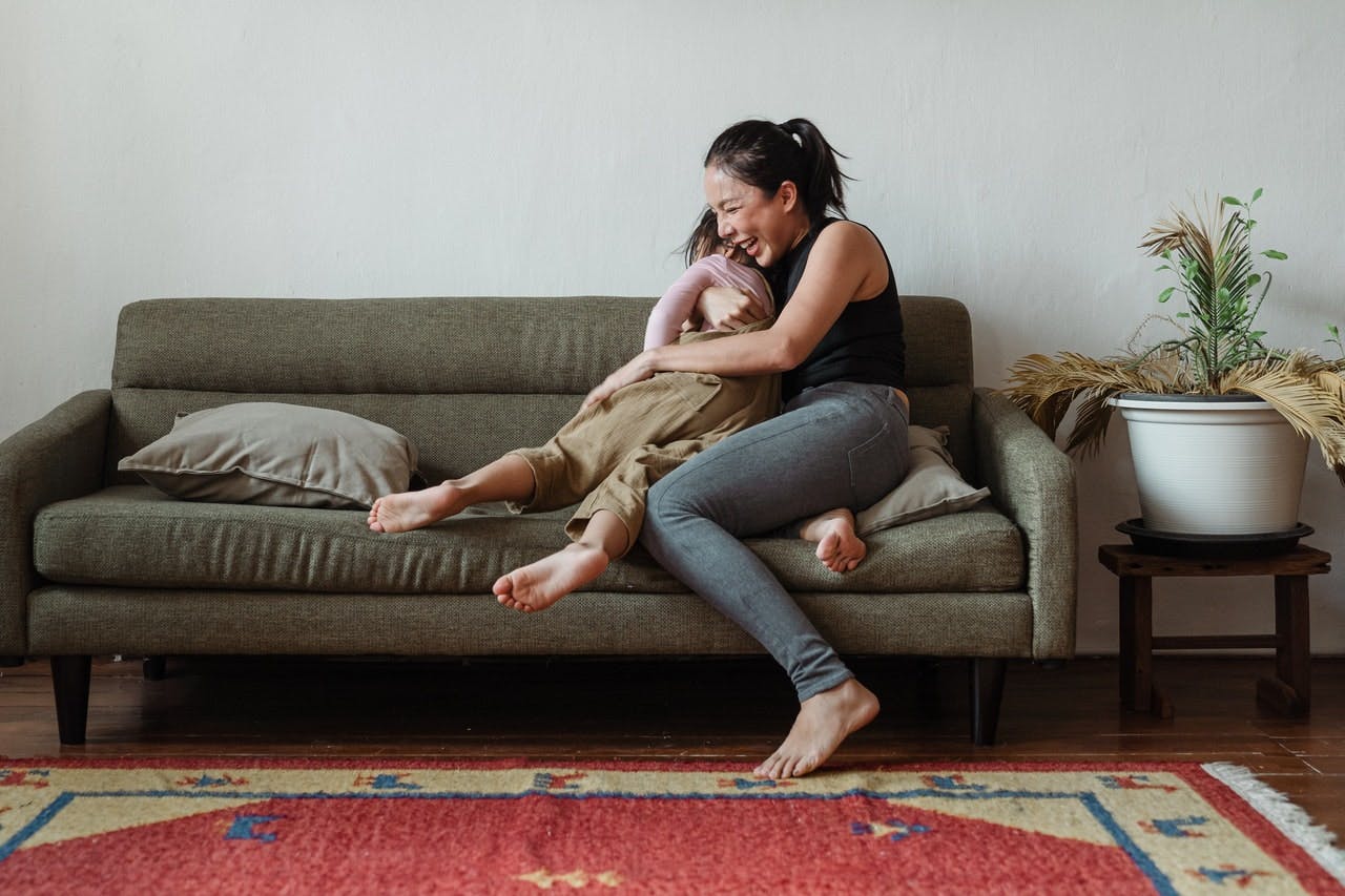 A very happy mother hugs child on a khaki sofa in comfortable living room