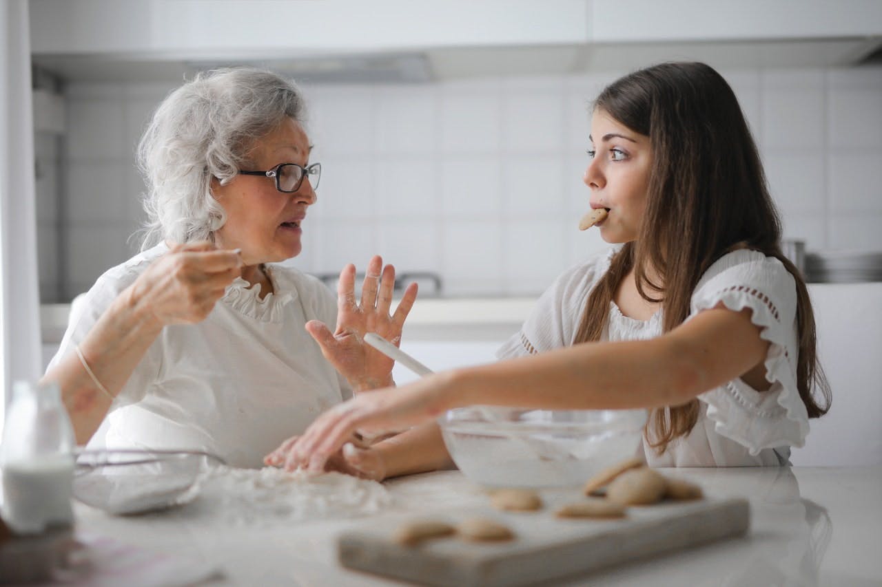 An older woman talks to a young girl whilst they bake cookies