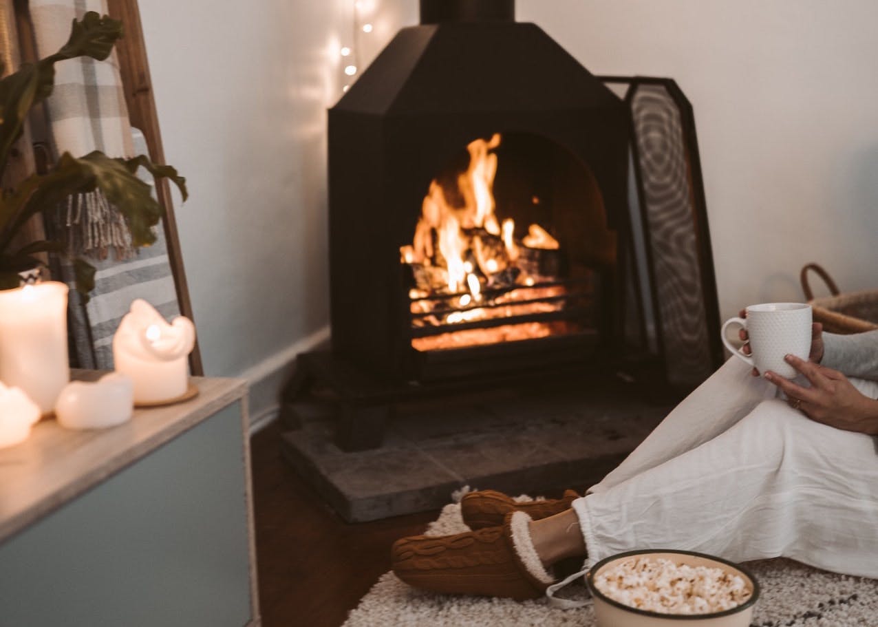 person holding a cup of tea in front of log burning fireplace in winter
