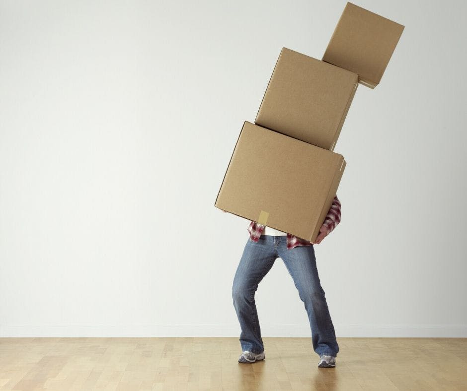 person in jeans carrying a stack of moving home cardboard boxes