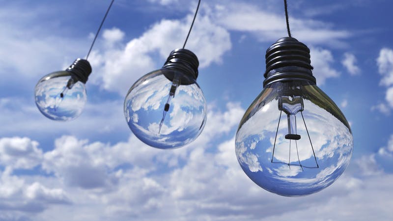 three light bulbs hanging in front of a blue sky with clouds