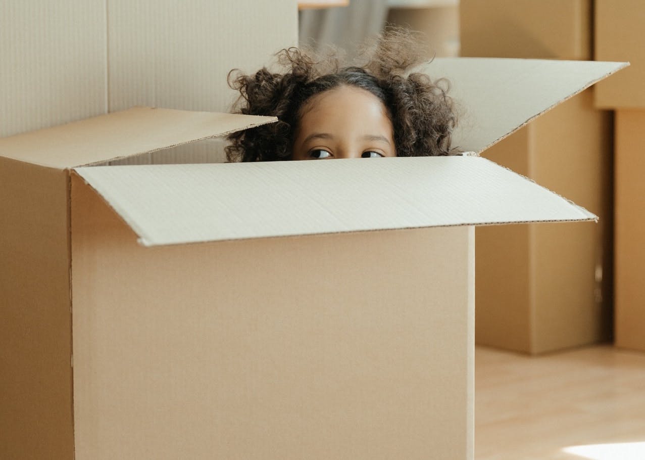 A young child hides in a cardboard box for moving house, their head sticks out the top 