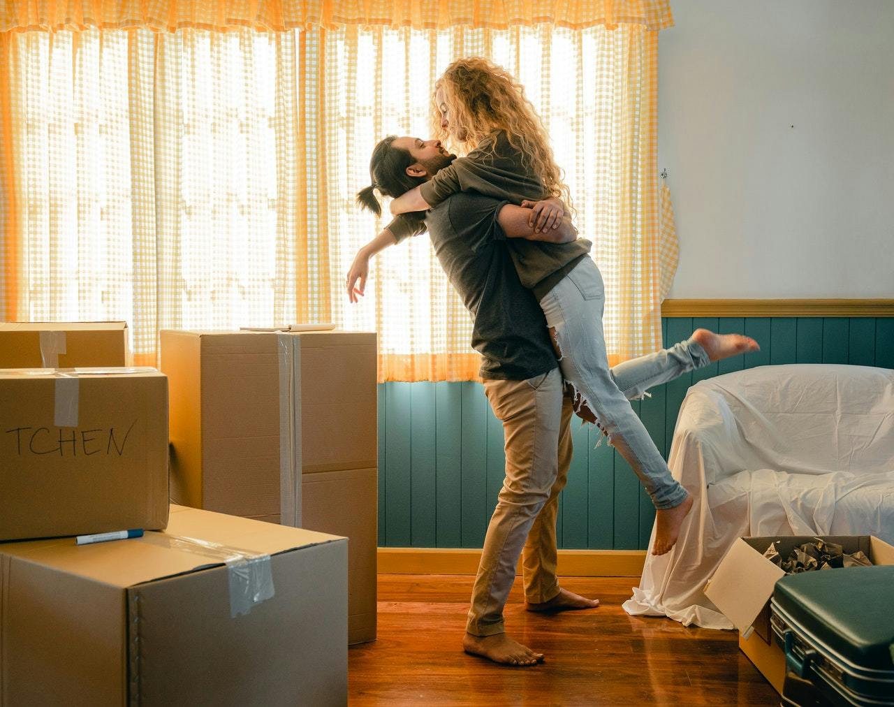 Man and woman hug each in a living room filled with packed moving boxes.