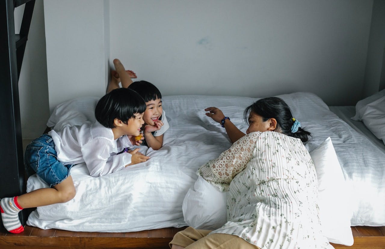 Mother lies on bed with two young children who are laughing