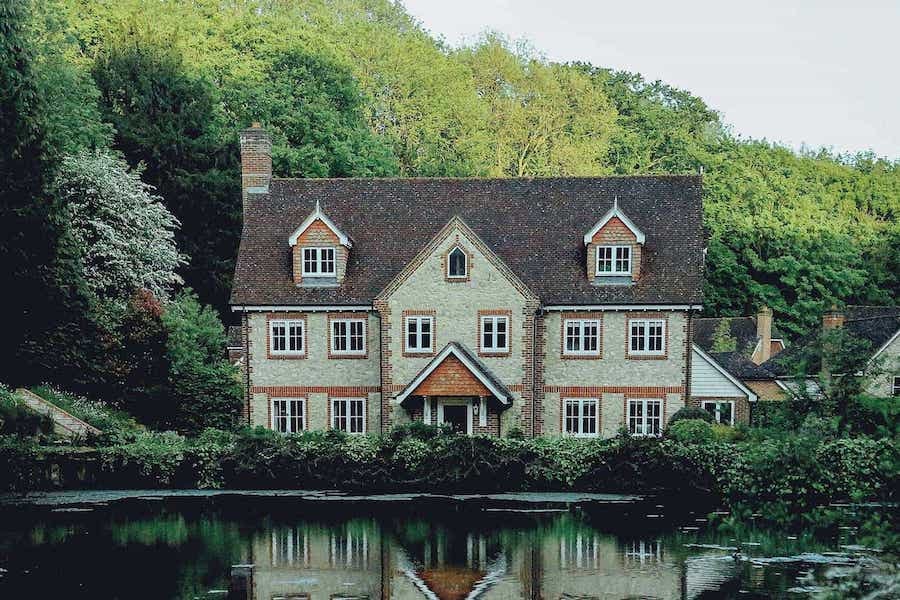 large stone house with attic windows sat by a lake in a forest in Spring