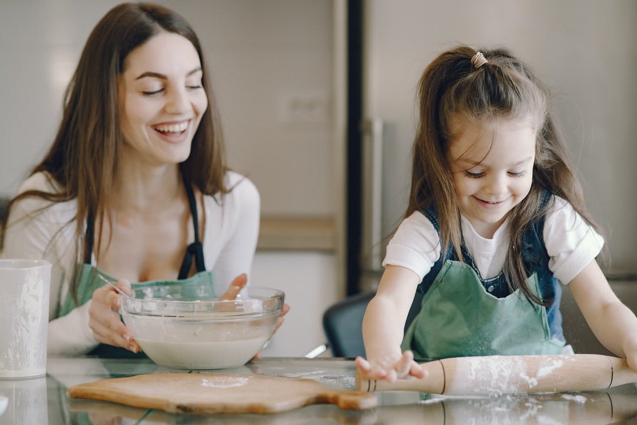 Young child and mother messily roll out biscuits in a modern kitchen