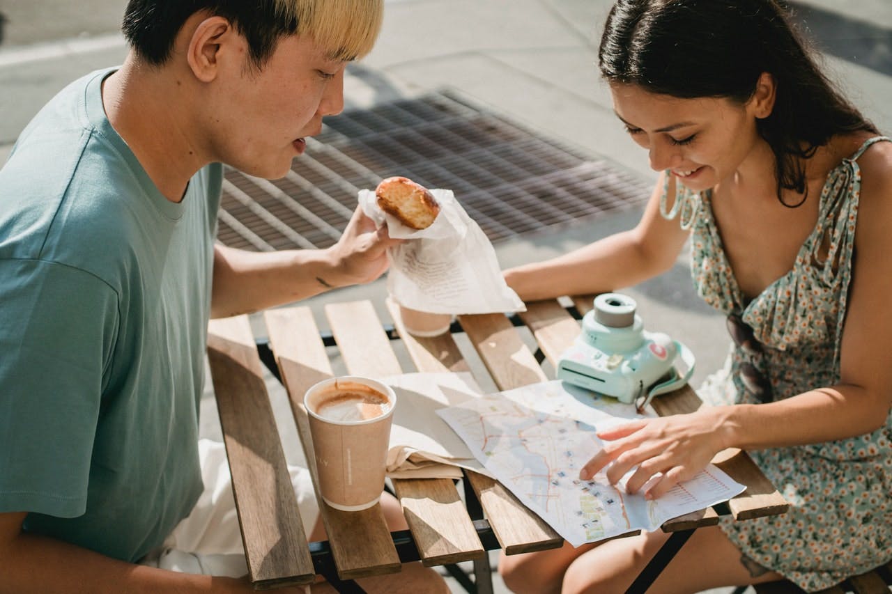 a man and a woman enjoy coffee and pastry whilst looking at a map of the city they've just moved to 