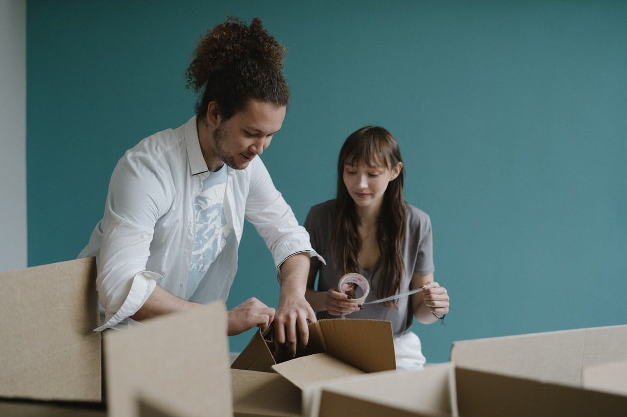 Man and woman in turquoise room pack moving boxes