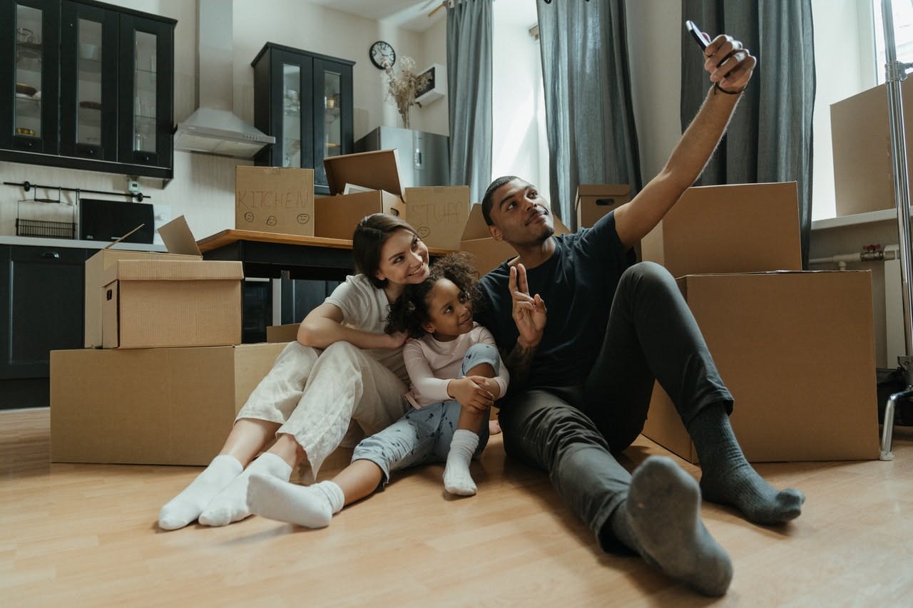 Young family celebrates moving house by taking selfie in kitchen filled with cardboard packing boxes