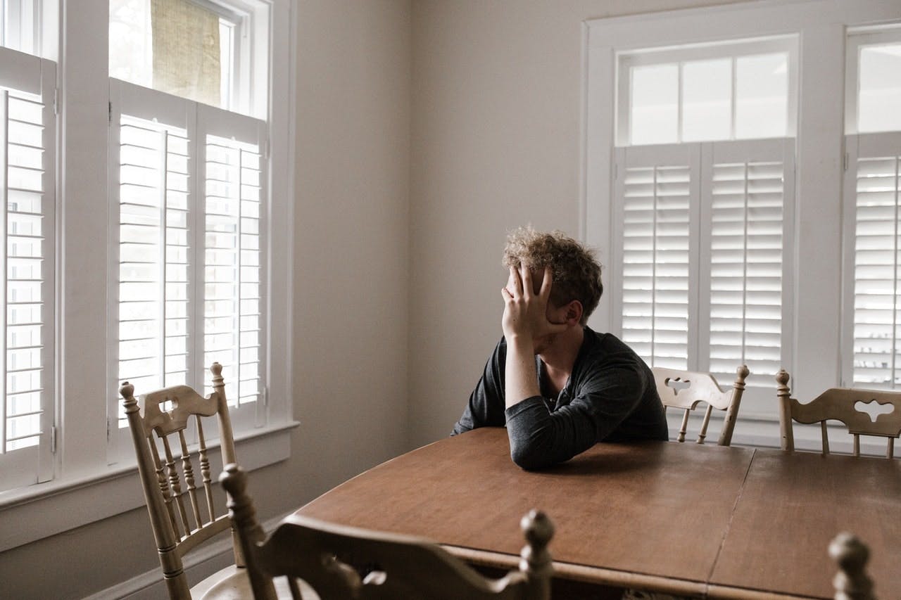 man sat at wooden dining table looks frustrated out of window
