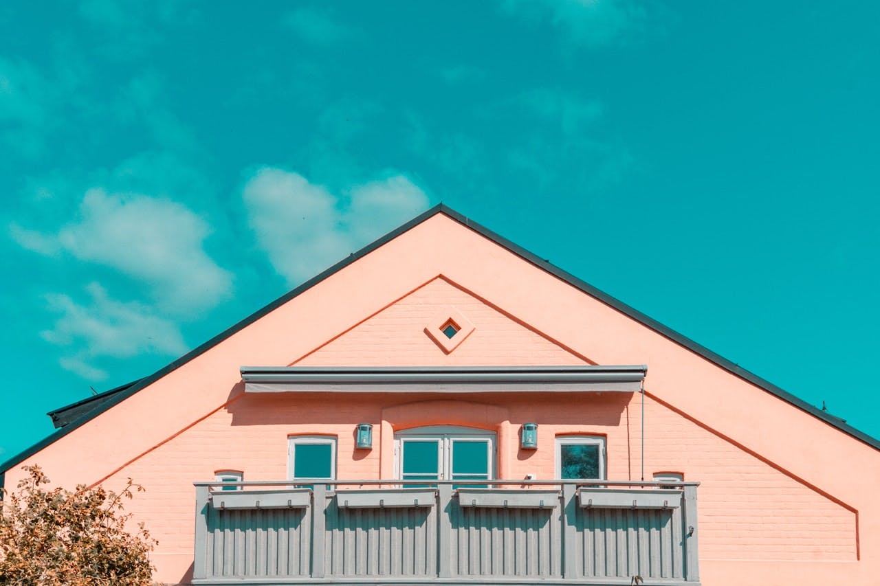 Detail of a salmon pink house with balcony, contrasting with a bright blue sky