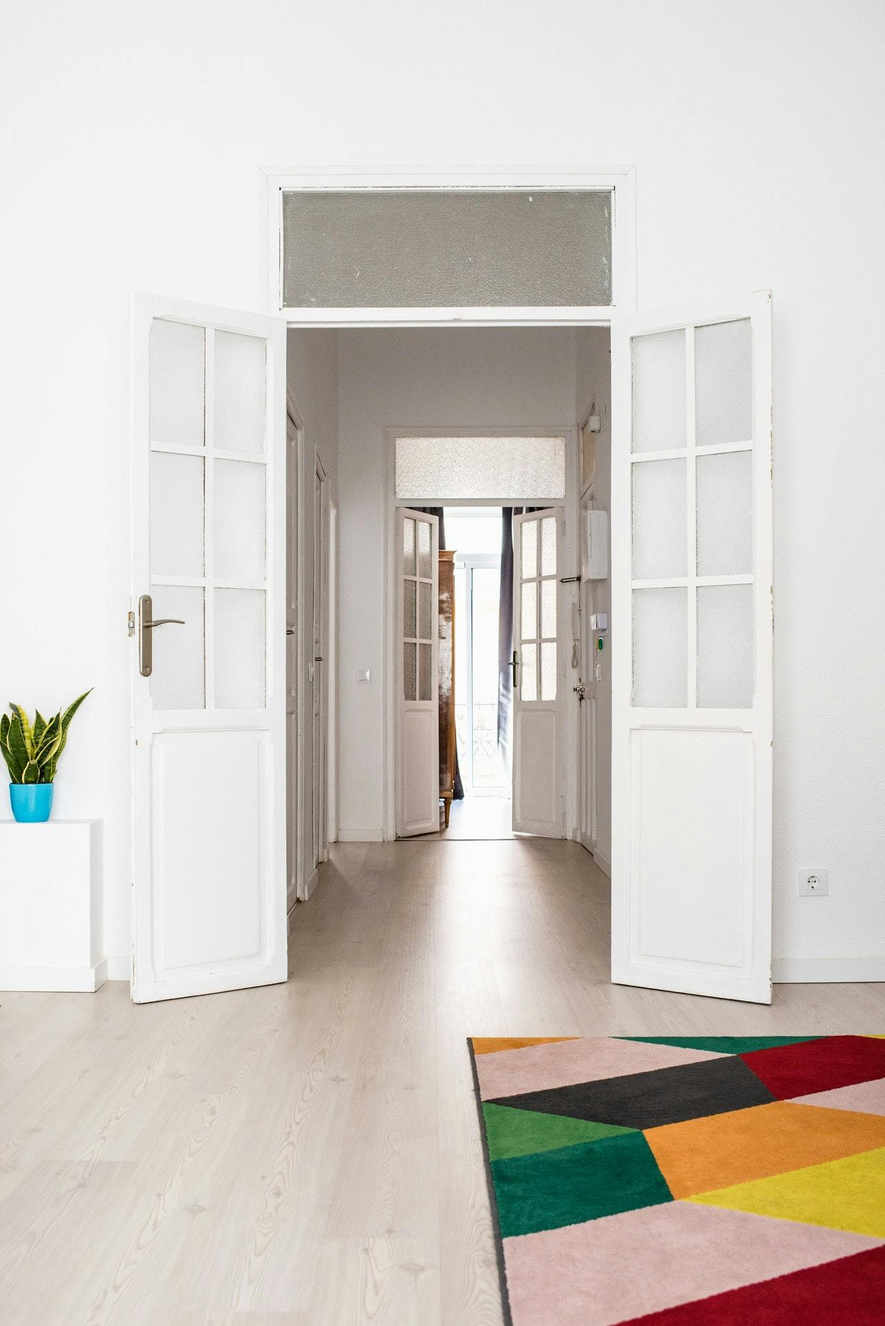 A hallway with two sets of open white doors with glass panels, a colourful rug on the floor