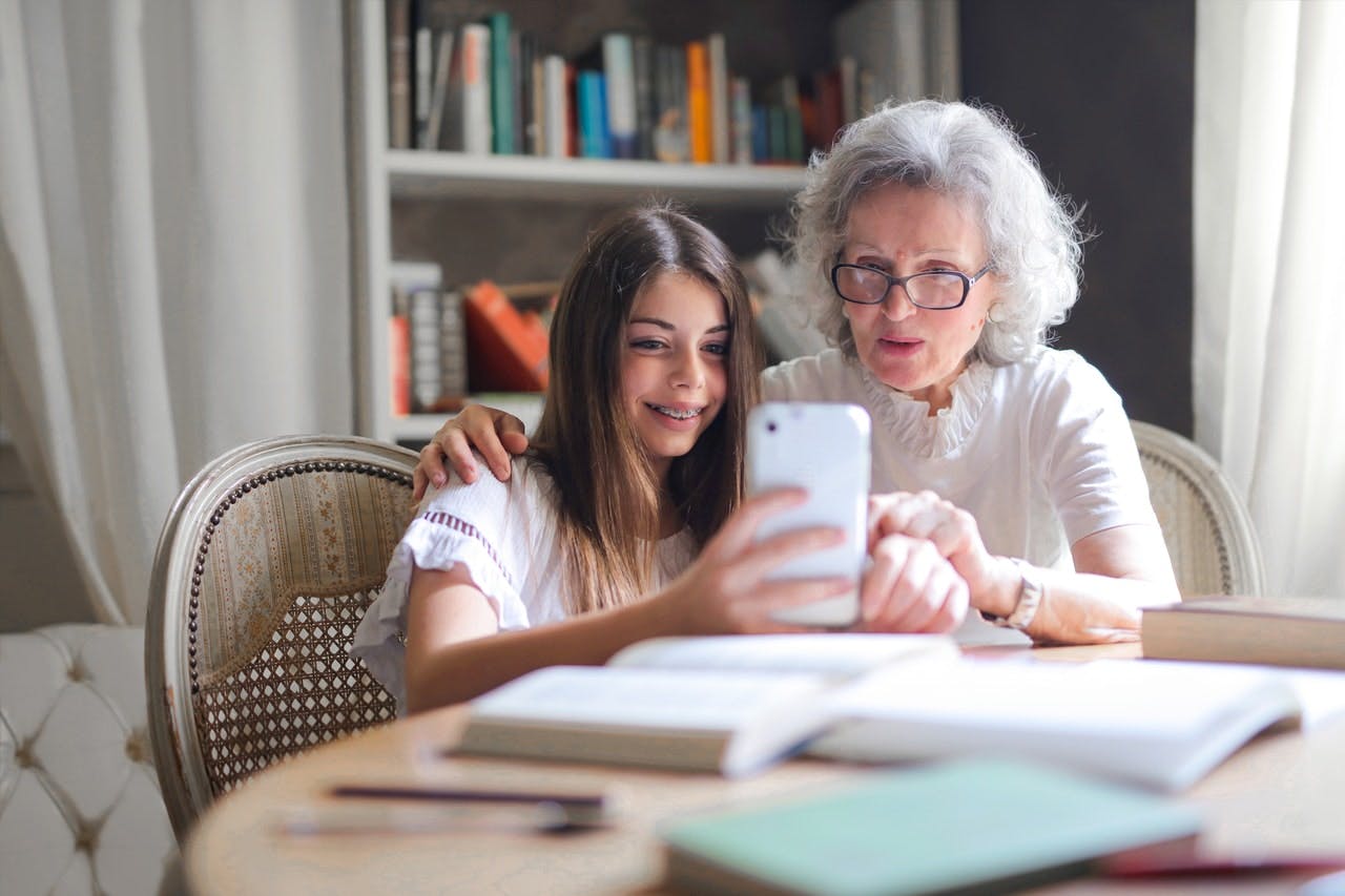 An older woman and young girl take a selfie while sat at a wooden table covered in books