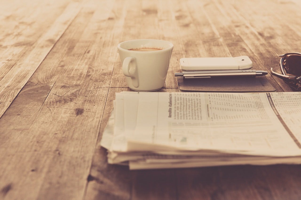 a folded newspaper lying next to a cup of coffee on a wooden table 