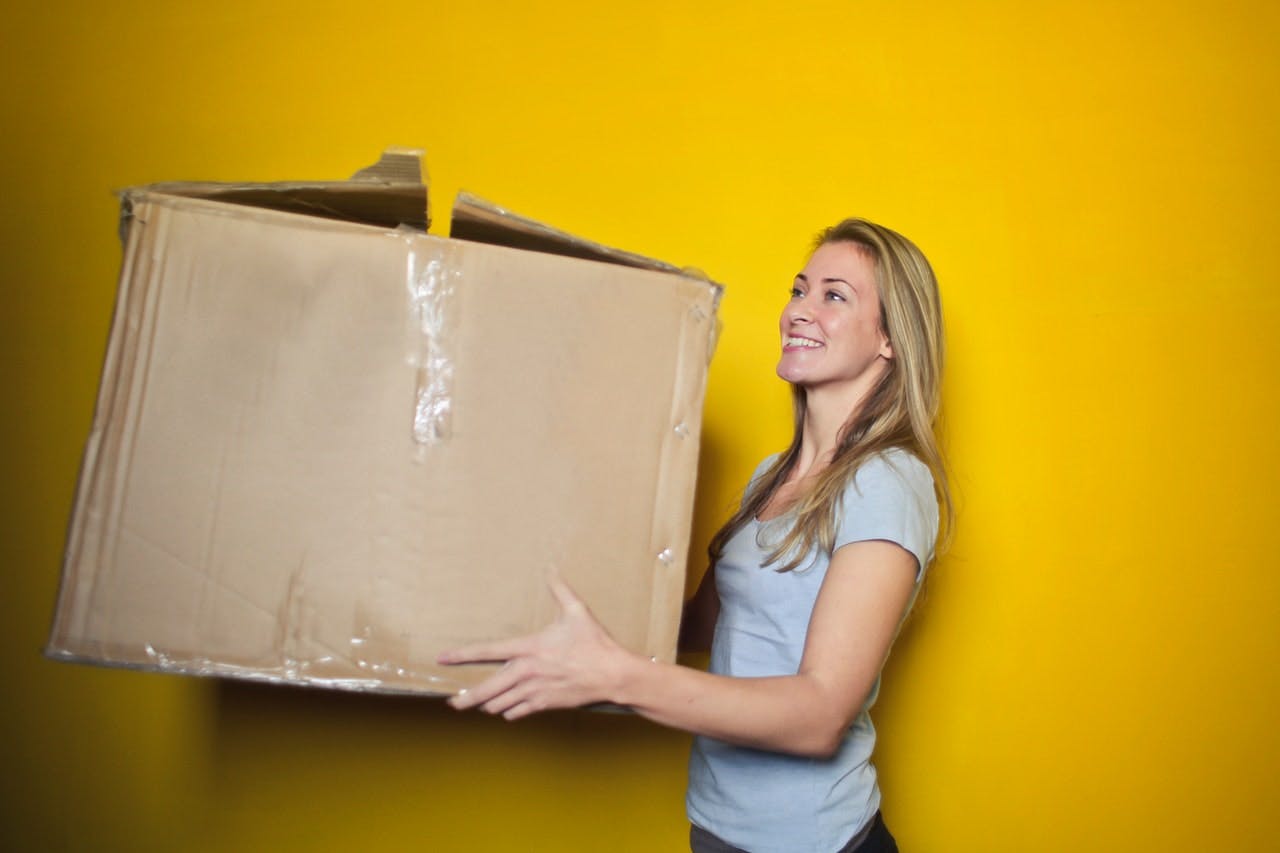 happy woman carries a cardboard moving box 