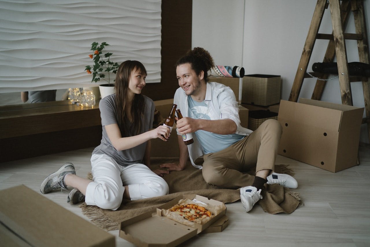 Couple celebrating their move with pizza and surrounded by cardboard boxes. 