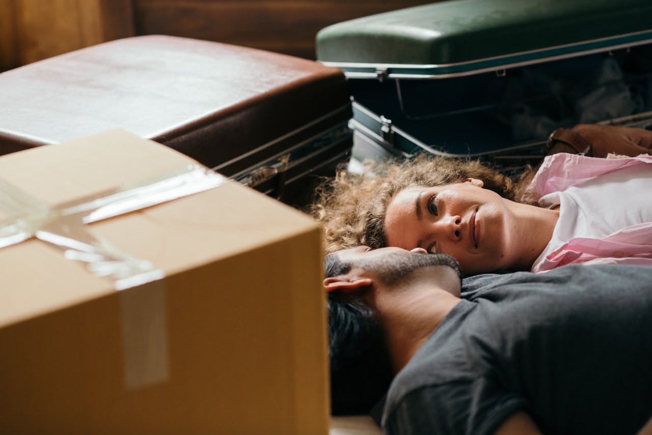 Two home movers lie on floor of new house surrounded by suitcases and boxes