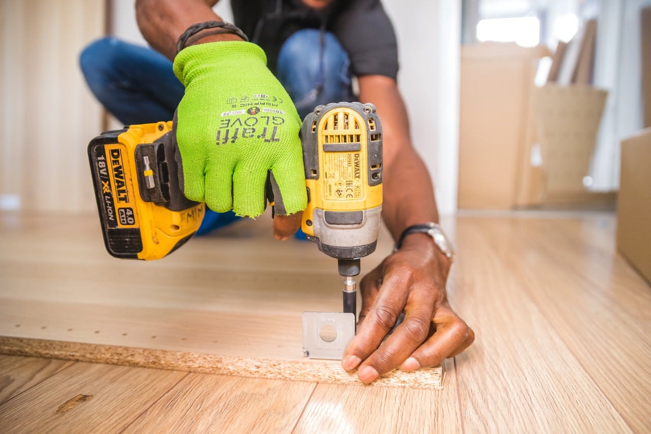 Person in green gloves uses drill to assemble wooden furniture