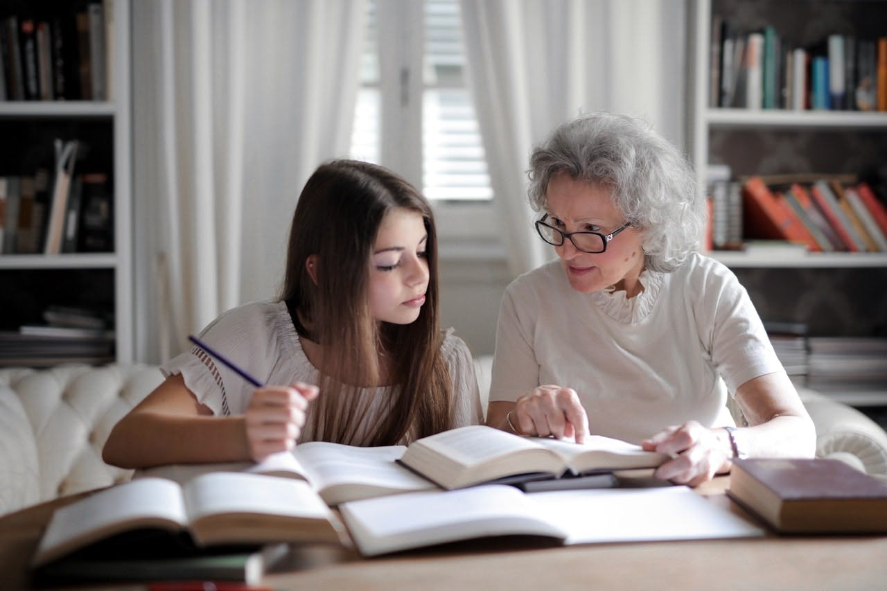 An older woman teaching a young girl history from books in a modern living room