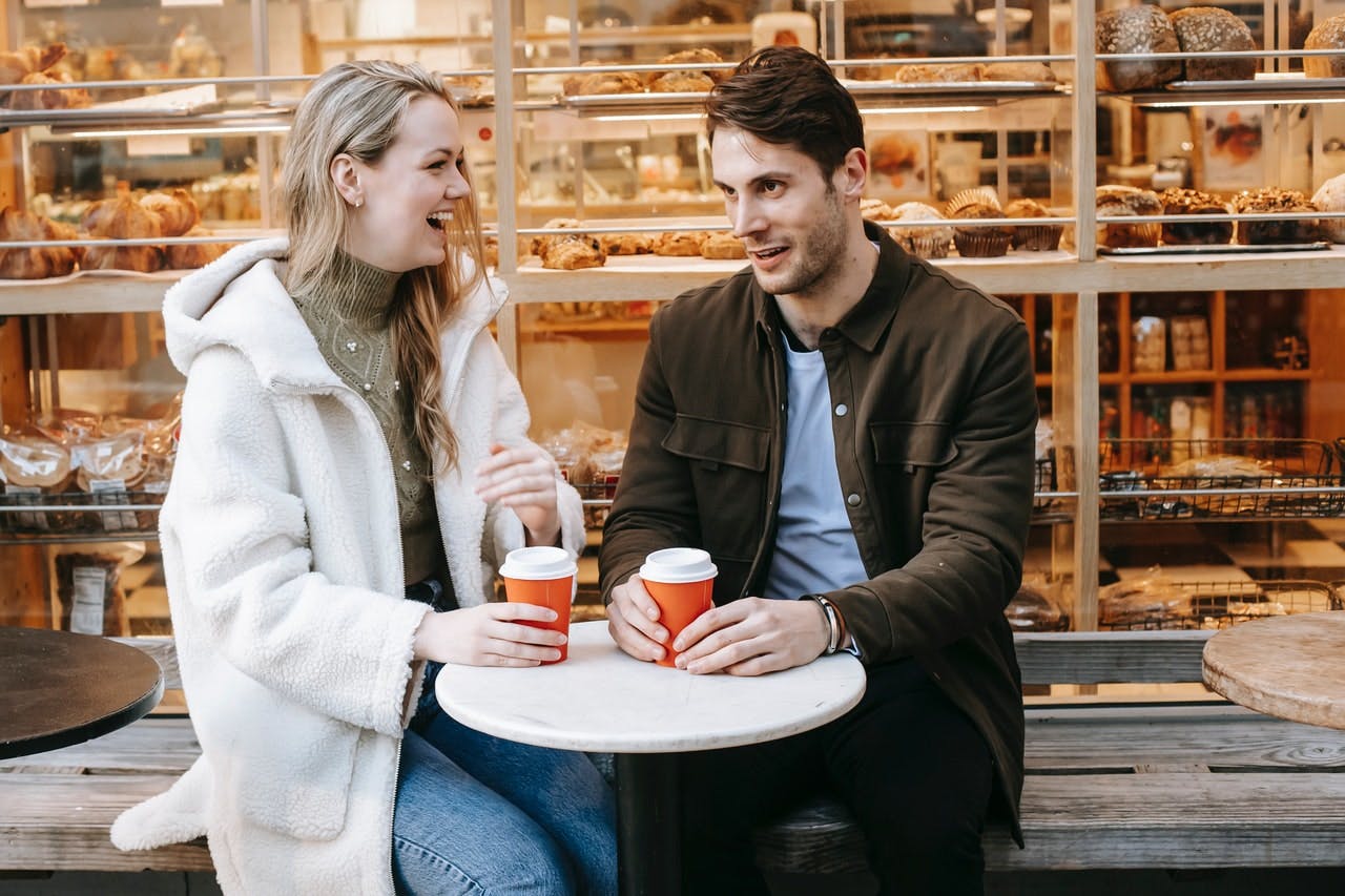 Young couple drinking takeaway coffee sit outside bakery