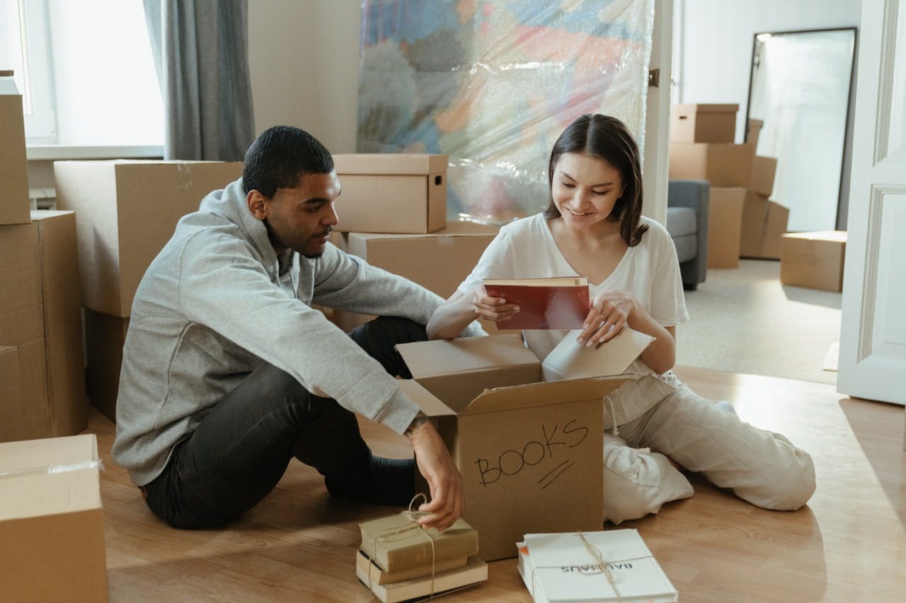 A man and a woman unpacking books from a cardboard box in their new home 