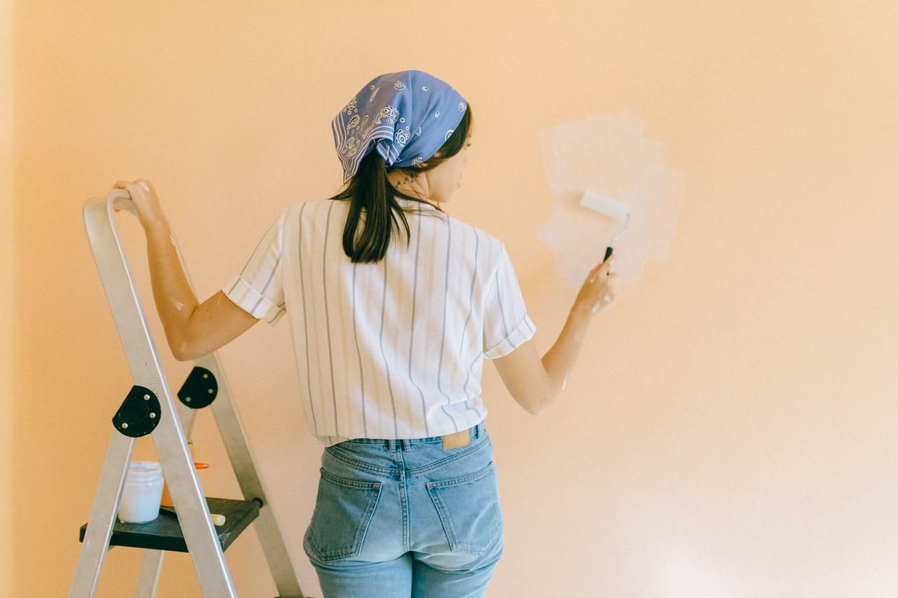 A woman using a roller to paint the wall of her home.