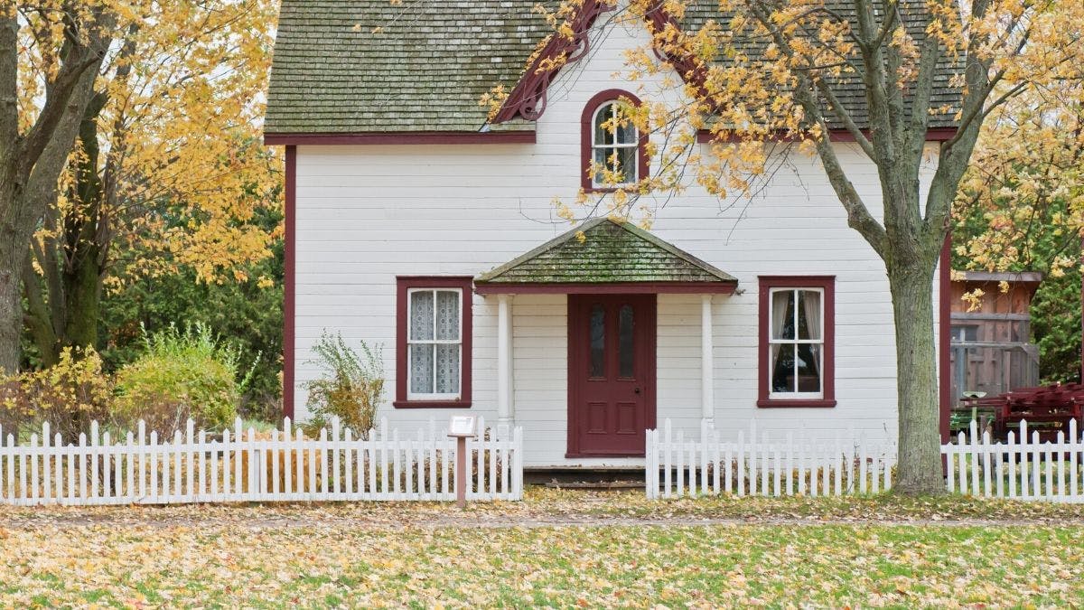 small wooden house with red door and window frames with garden and autumnal leaves