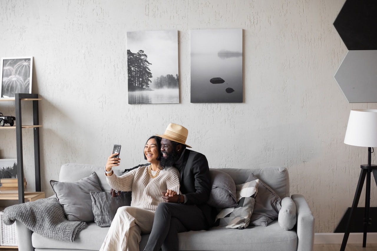 couple sat on grey sofa take a selfie in their new home 