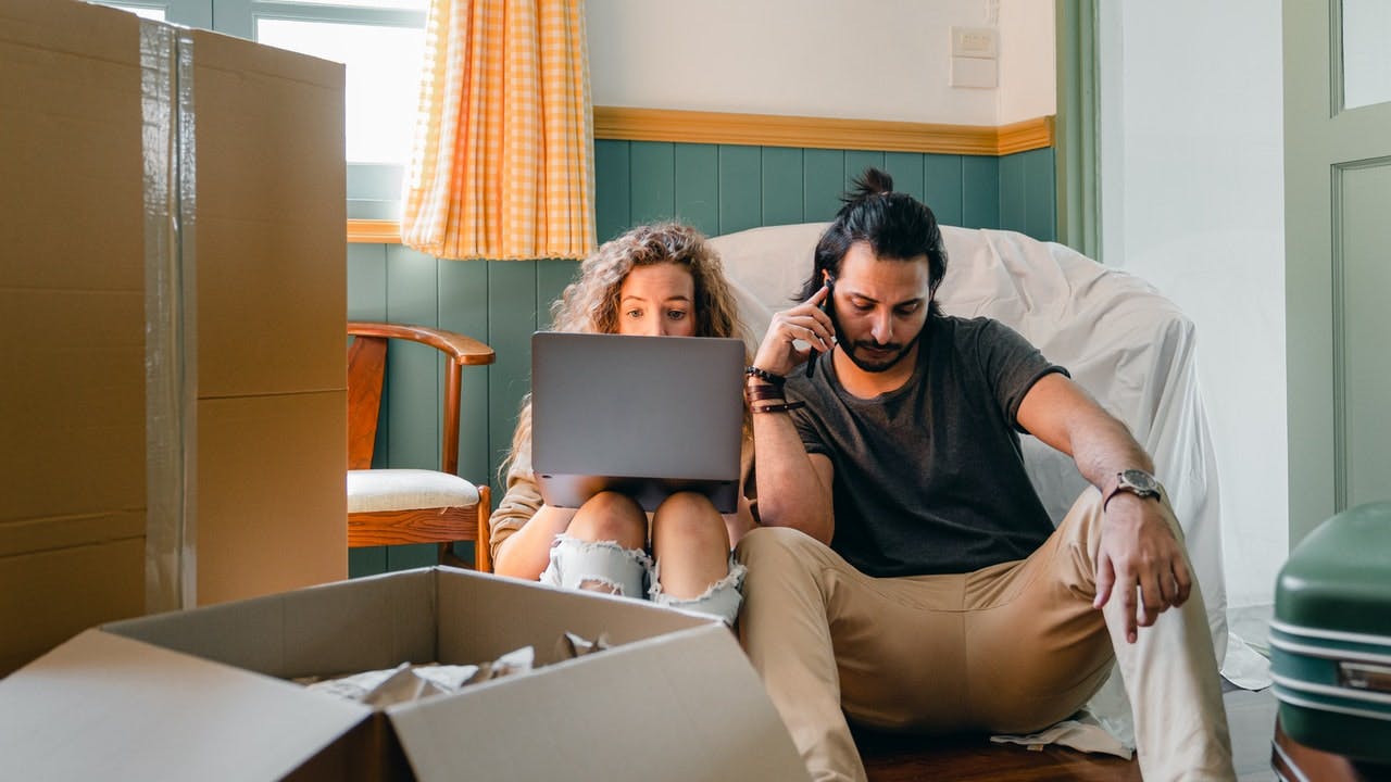 Homeowners sitting in a room with packed boxes looking at a laptop screen.