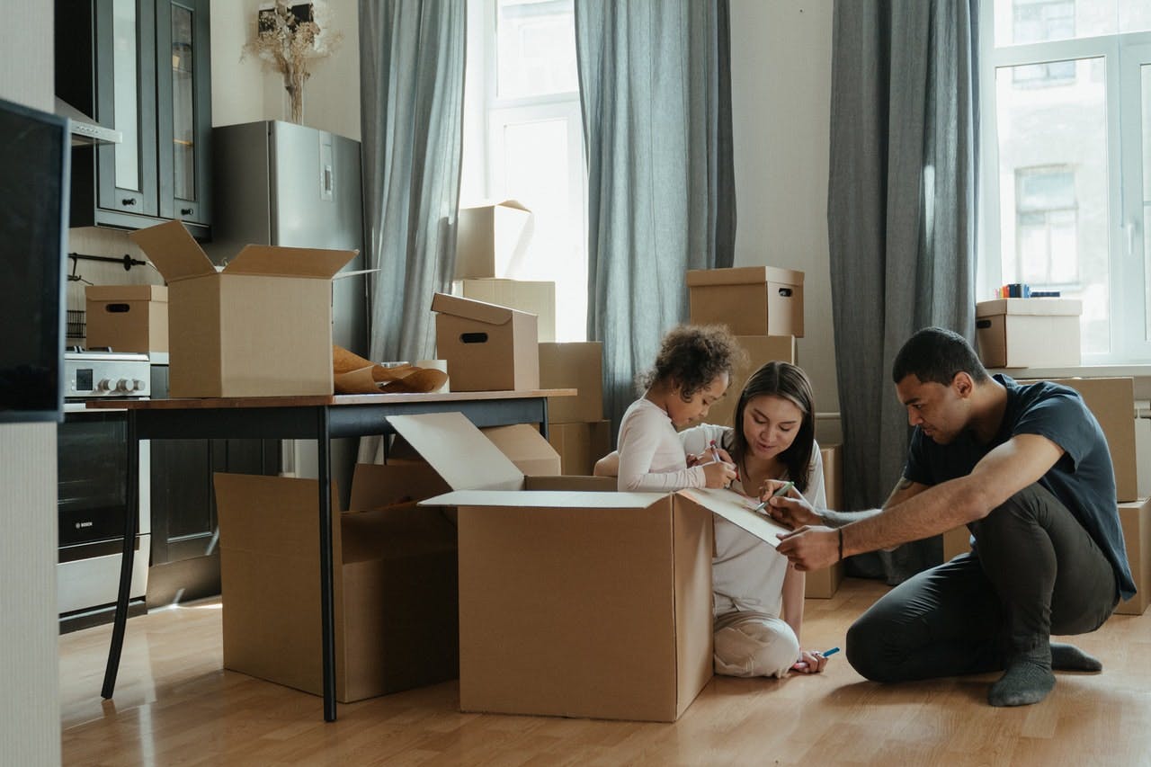 Family label home moving boxes in kitchen whilst young child sits inside one of the boxes